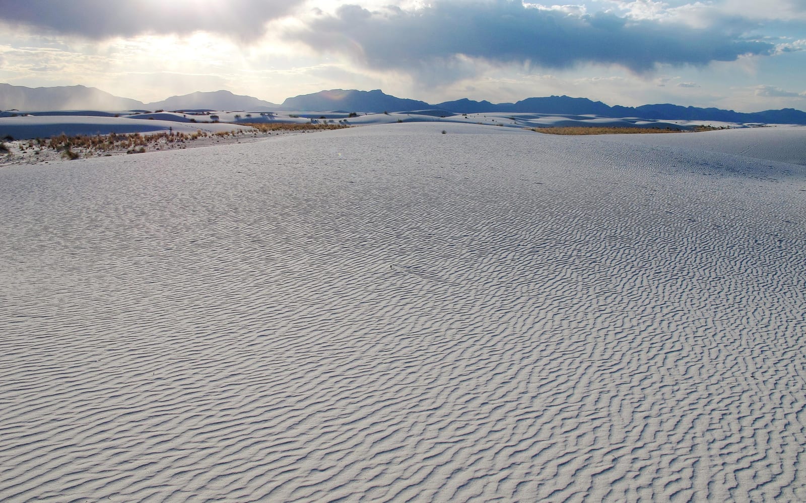 White dunes in foreground with sun setting behind mountain.