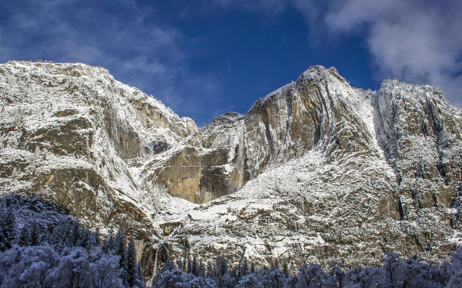 Two tall waterfalls flowing down snow covered granite walls.